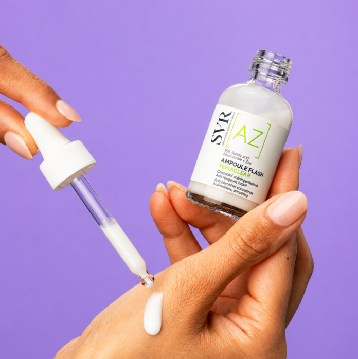 site-industries-cosmetiques A person holds a glass dropper above his hand, dispensing a white serum from a clear bottle labeled 