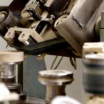 site-industries-cosmetiques Vista de perto de uma máquina de trabalhar madeira automatizada que dá forma a peças circulares de madeira, com um emblema "25 anos de beleza na madeira" no canto superior direito.