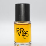 site-industries-cosmetiques Um pequeno frasco de vidro transparente cheio de um líquido amarelo, encimado por uma tampa preta. A garrafa tem a palavra "PARADES" impressa a preto, com letras espelhadas na parte da frente. A base é branca.