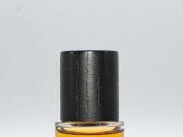 site-industries-cosmetiques 一个装满黄色液体的透明小玻璃瓶，瓶盖为黑色。瓶身上印有黑色的 "PARADES "字样，正面印有镜面字样。瓶底为白色。.