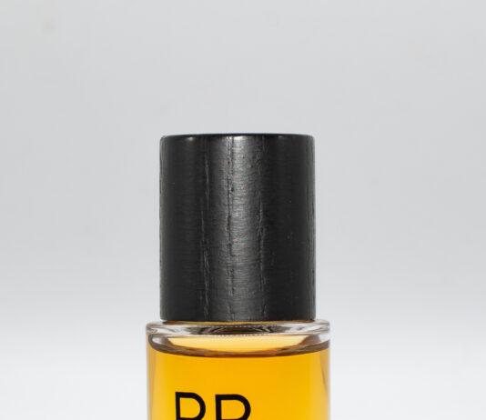 site-industries-cosmetiques 一个装满黄色液体的透明小玻璃瓶，瓶盖为黑色。瓶身上印有黑色的 "PARADES "字样，正面印有镜面字样。瓶底为白色。.