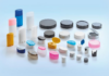 site-industries-cosmetiques Sobre un fondo azul claro, diversos recipientes de plástico, tapones y tapas de diferentes formas, tamaños y colores. Algunos son cilíndricos, otros ovalados o planos.