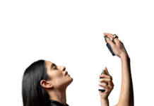 site-industries-cosmetiques Une femme aux longs cheveux noirs et vêtue d'un haut noir sans manches s'asperge de parfum, tenant le flacon près de son cou et regardant vers le haut, sur un fond blanc uni.