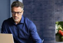 site-industries-cosmetiques Un homme portant des lunettes et une chemise bleue travaille sur un ordinateur portable. Dans le coin inférieur droit, une image plus petite montre des fraises poussant sur un plant, avec une baie rouge mûre et deux vertes.