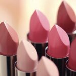 site-industries-cosmetiques Varios tubos de pintalabios en diferentes tonos de rosa y nude están dispuestos uno al lado del otro, con los extremos hacia arriba. El fondo está ligeramente difuminado.
