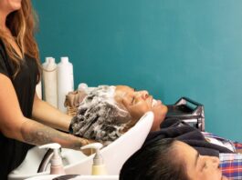 site-industries-cosmetiques Duas pessoas estão sentadas nas estações de lavagem do salão, com as cabeças inclinadas para trás, enquanto um estilista lava o cabelo de uma delas. Ambos os clientes parecem descontraídos. Ao fundo, vêem-se frascos de produtos para o cabelo.