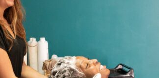 site-industries-cosmetiques 两个人坐在发廊的洗头台前，头向后仰，发型师正在为其中一人洗头。两位顾客看起来都很放松。背景中可以看到美发产品的瓶子。.
