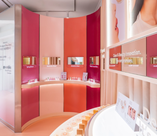 site-industries-cosmetiques A modern display area dedicated to beauty products features curved walls in shades of pink and orange, shelves displaying skincare products, digital screens above each shelf, and promotional posters hanging on the wall. Bright, even lighting highlights the entire space.