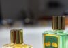 Piver opta por un capó de zamak con acabado de cataforesis dorada site-industries-cosmetiques Tres frascos de perfume de cristal con tapones dorados se presentan sobre una superficie blanca. Dos frascos están en posición vertical y contienen un líquido amarillo y verde, mientras que un tercer tapón descansa de lado en primer plano.