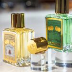 Piver opta por um capot em zamak com acabamento em cataforese dourada site-industries-cosmetiques Três frascos de perfume em vidro com tampas douradas são apresentados numa superfície branca. Dois frascos estão na vertical, contendo um líquido amarelo e verde, enquanto uma terceira tampa está de lado, em primeiro plano.