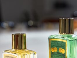 site-industries-cosmetiques Tres frascos de perfume de cristal con tapones dorados se presentan sobre una superficie blanca. Dos frascos están en posición vertical y contienen un líquido amarillo y verde, mientras que un tercer tapón descansa de lado en primer plano.
