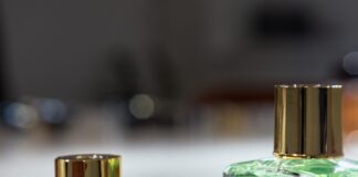 site-industries-cosmetiques 在白色的表面上摆放着三个带金色瓶盖的玻璃香水瓶。两个瓶子直立着，里面装着黄色和绿色的液体，而第三个瓶盖则侧放在前景中。.