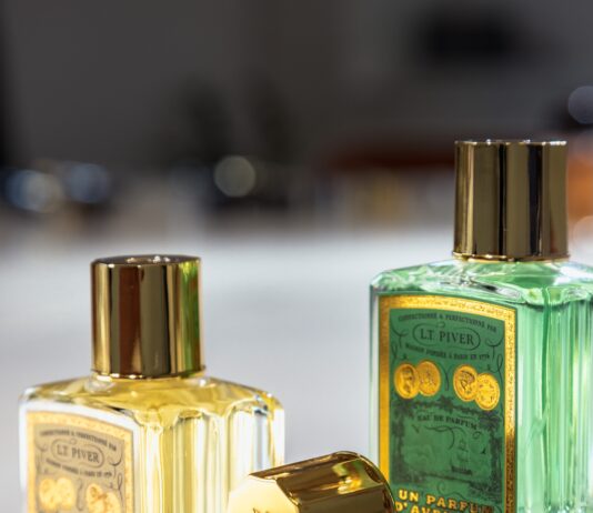 site-industries-cosmetiques Tres frascos de perfume de cristal con tapones dorados se presentan sobre una superficie blanca. Dos frascos están en posición vertical y contienen un líquido amarillo y verde, mientras que un tercer tapón descansa de lado en primer plano.