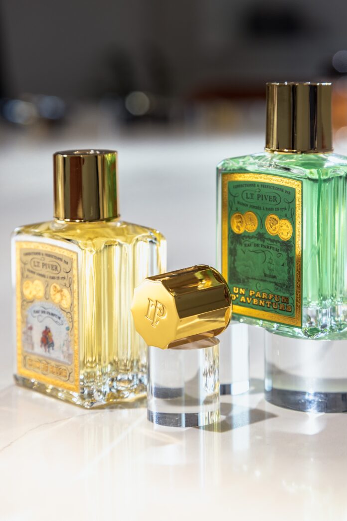 site-industries-cosmetiques Tres frascos de perfume de cristal con tapones dorados se presentan sobre una superficie blanca. Dos frascos están en posición vertical y contienen un líquido amarillo y verde, mientras que un tercer tapón descansa de lado en primer plano.