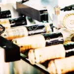 site-industries-cosmetiques 在自动化生产线上为带瓶塞的酒瓶贴标签的机器特写。在贴标过程中，酒瓶通过滚筒和齿轮移动。.