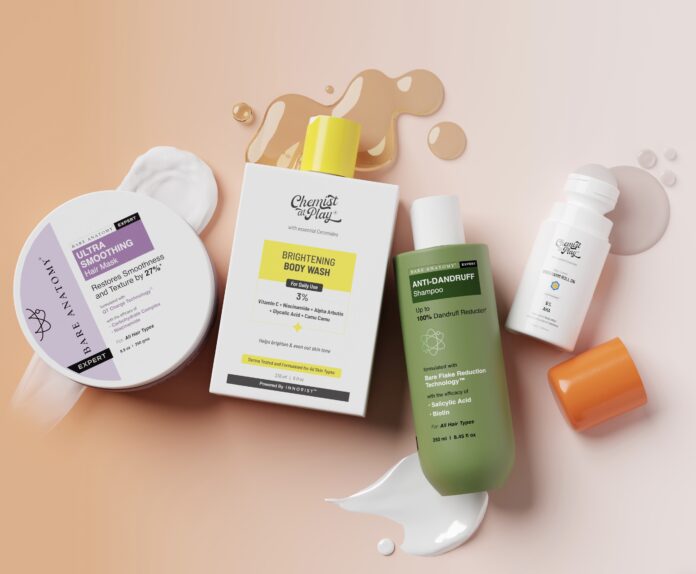 site-industries-cosmetiques 一组由五款护肤及护发产品组成的«平铺»摆拍，包括面霜、沐浴露、 一款洗发水以及一瓶配有橙色瓶盖的瓶子，这些产品陈列在粉色背景上，周围散落着产品残留痕迹和液体飞溅的痕迹。.