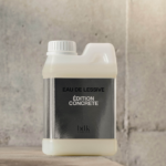 BDK Parfums lanza el «Eau de Lessive» Edición Concrète site-industries-cosmetiques Un recipiente de plástico con un tapón de rosca blanco descansa sobre una superficie de hormigón. La etiqueta lleva la inscripción «EAU DE LESSIVE ÉDITION CONCRÈTE bdlk» en letras blancas sobre fondo negro. Al fondo se ve la pared de hormigón.
