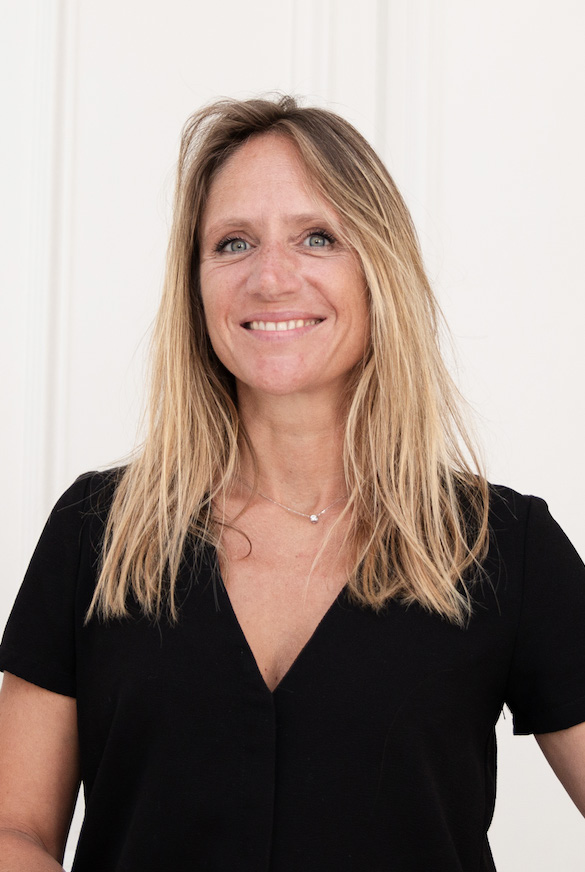 BDK Parfums Launches Eau de Lessive Édition Concrète 1 site-industries-cosmetiques A woman with long blonde hair, wearing a black V-neck top, is standing in front of a light-colored background and smiling at the camera.