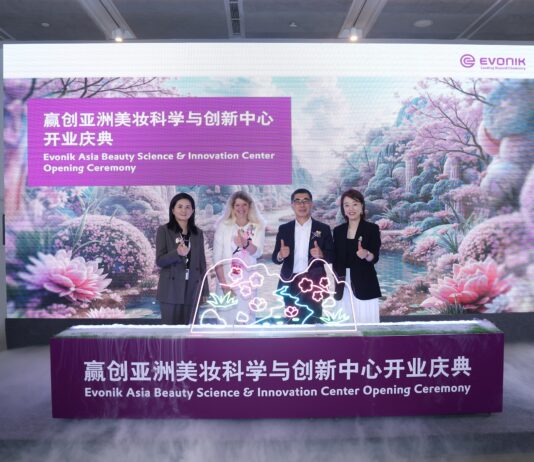 site-industries-cosmetiques Quatro pessoas estão de pé atrás de um pódio decorado com luzes na cerimónia de abertura do Evonik Asia Beauty Science & Innovation Center, em frente a uma exposição de flores e a um cartaz com o nome do evento em inglês e chinês.