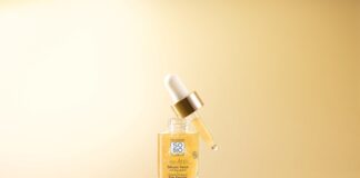 site-industries-cosmetiques Un frasco de cristal transparente que contiene el sérum para los ojos SO'BIO étic, provisto de un gotero dorado y blanco, colocado sobre una superficie de color marrón claro, con dos nueces de argán marrones a su lado, todo ello sobre un fondo beige a juego.