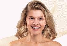 Liftilience pour cheveux texturés: données d’efficacité capillaire site-industries-cosmetiques Une femme aux cheveux blonds mi-longs sourit à la caméra devant un fond clair orné de lignes ondulées beiges. Elle a le teint clair et est photographiée de la tête aux épaules.