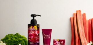 site-industries-cosmetiques Un flacon, un tube et un coffret de produits de soins personnels Floral Street sont disposés sur une surface claire, avec en arrière-plan des fleurs, un demi-citron, des feuilles vertes et des tiges de rhubarbe.