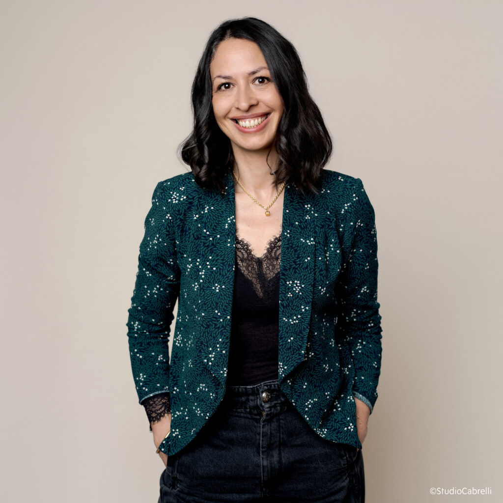 65 % of French people suffer from foot problems... 1 site-industries-cosmetiques A woman with medium-length dark hair smiles at the camera. She is wearing a dark green patterned blazer over a black lace top and black pants; barefoot, she is caring for her feet against a plain light beige background.
