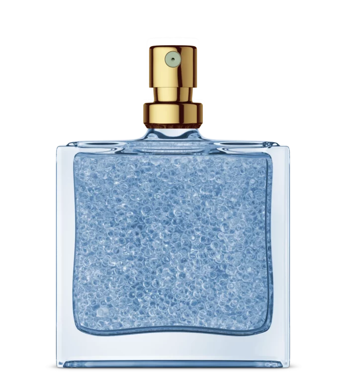 site-industries-cosmetiques Un frasco de perfume cuadrado de cristal, provisto de un pulverizador dorado y relleno de perlas de gel azules creadas mediante la tecnología de encapsulación Microcaps, destaca sobre un fondo blanco liso.