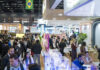 FCE 2026: récord de expositores y rumbo a la cosmetología site-industries-cosmetiques Una numerosa multitud pasea y charla en una feria profesional o una exposición muy animada que se celebra en un recinto cerrado. Los pasillos están flanqueados por stands y expositores, y una bandera brasileña ondea sobre la multitud. Los visitantes visten ropa de trabajo o informal.