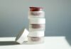 Arena Glass Refill Jar: a 60 ml refillable glass jar with a 50 ml insert site-industries-cosmetiques A stack of three frosted jars labeled «Arena Glass Relief 2.0,» one of which has its white lid removed and placed next to it, against a plain background bathed in natural light.