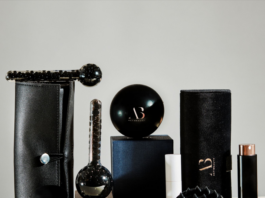 site-industries-cosmetiques 一套黑色和棕色的男士美容或护理产品系列，包括一款带有纹理的按摩工具、圆形容器、圆柱体、 一把刷子以及两个皮革或人造革材质的收纳盒，陈列于纯色背景的素色基面上。.