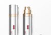 Lumson designs the packaging for Lancôme's Absolue Longevity MD site-industries-cosmetiques Two silver bottles of anti-aging cream—one with a closed cap and the other with an exposed pump—are placed on a white surface. A silver cap decorated with a rose motif is placed next to them. The labels show the product name and the brand name.