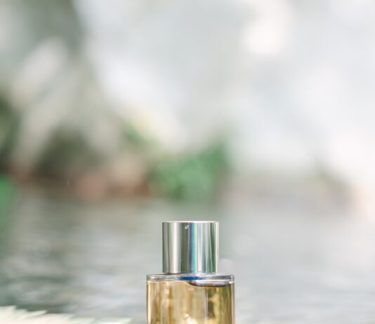 site-industries-cosmetiques 一只透明玻璃香水瓶，配有银色瓶盖，静静地置于一块半浸没在浅溪中的岩石上。背景略显模糊，沐浴在室外的自然光线下。.
